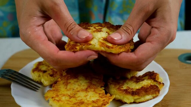 Woman showing cooked fried potatoes pancakes, draniki on plate on kitchen at home, hands close-up. Preparing fresh dish. Cuisine, culinary, recipe. Traditional Russian food on lunch dinner.