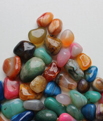 Colored rough gemstones in a triangle heap on white surface detailed top view 