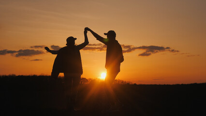 Two farmers dance merrily in a field. Silhouettes against the sky where the sun sets