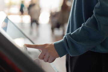 man at self service transfer area doing self-check-in or buying plane tickets at automated machine with touchscreen interactive display in modern airport terminal building