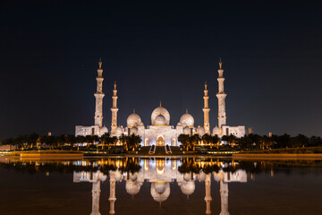 Grand Sheikh Zayed Mosque with illuminated minarets and domes reflected on water at night