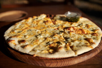 A delicious round pizza on a wooden tray with pesto sauce. A process of tasting eating traditional italian four cheeses pizza in outside restaurant terrace.Simple snack.Unhealthy food.Nutrition rules