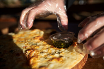 A delicious round pizza on a wooden tray with pesto sauce. A process of tasting eating traditional italian four cheeses pizza in outside restaurant terrace.Simple snack.Unhealthy food.Nutrition rules