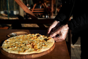 A delicious round pizza on a wooden tray with pesto sauce. A process of tasting eating traditional italian four cheeses pizza in outside restaurant terrace.Simple snack.Unhealthy food.Nutrition rules