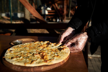 A delicious round pizza on a wooden tray lying on table.Hands picking up a slice of traditional...
