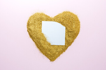 Heart shape made of gold glitter with blank paper card. Flat lay. Love concept.