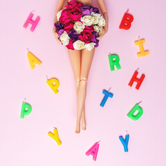 Girl doll with colorful flowers and birthday candles on pink background. Creative minimal holiday concept.