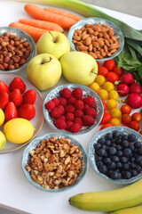 Apples, lemons, bananas, berries, carrots, leek, tomatoes, radishes, spinach and various nuts on white background. Healthy seasonal fruit and vegetable. Selective focus.