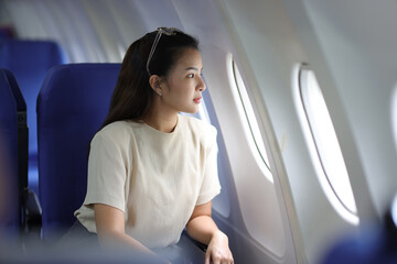 Lonely Asian female tourist traveling alone on a plane looking out the window, She is thinking of...