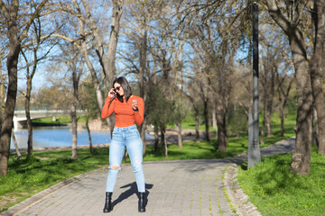 Young and beautiful brunette woman dressed in casual clothes and sunglasses, walks along a path between deciduous trees in autumn, in the background a lake.