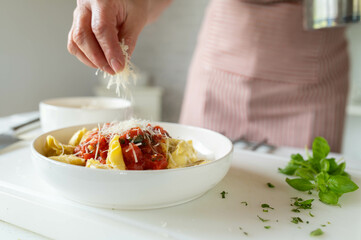 Sprinkling fresh grated parmesan cheese over a homemade pasta dish with tomato sauce