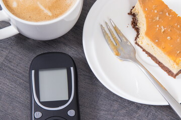Glucose meter, sweet cheesecake and cup of coffee with milk. Measuring and sugar level control during diabetes