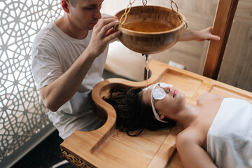 High-angle view of pouring oil on female forehead during exotic Shirodhara treatment, Ayurvedic healing technique . Serene young woman at massage session with aromatic oil dripping on forehead.