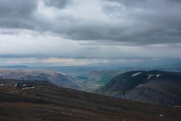 Dramatic top view from precipice edge to wide colorful valley and mountain silhouettes in rain...