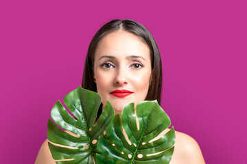 Beautiful young woman with a palm leaf on a bright background.