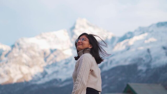 Portrait of happy Indian girl portrait. Girl standing against snow mountains in Lahaul, Himachal Pradesh, India. Tourist enjoying holiday trip in mountains. Solo traveler, backpacking concept.