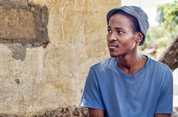 young village african man sited in front of the house in the yard, casual clothing with a striped...