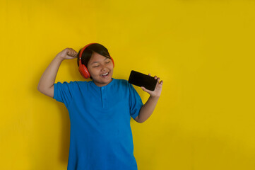 Happy Asian little girl in headphones sings favorite song and uses mobile phone as microphone.