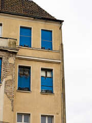 Broken windows of an abandoned residential building. Pigeons sitting in holes of the facade. The exterior of the property is weathered and run down due to poverty in the region.