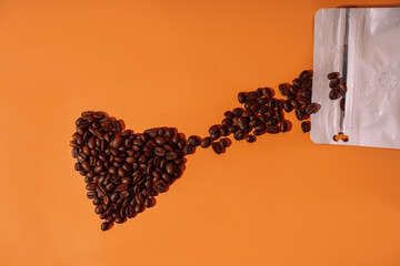 Coffee beans in the shape of a heart on an orange background spill out from a package.