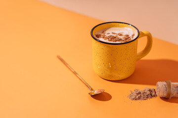 Yellow mug with coffee and cinnamon on an orange background with a spoon.