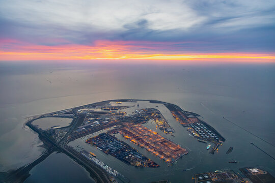 Aerial airplane view of Rotterdam sea port terminal, with many docks, ships and quay's in manmade harbour into the sea, ocean during bright colourful sunset