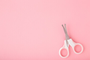 Scissors for baby nail cutting on light pink table background. Pastel color. Closeup. Empty place for text. Top down view.