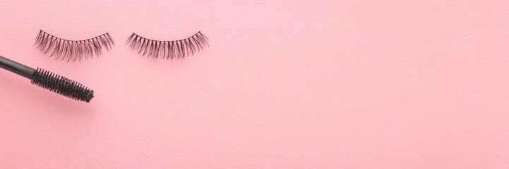 Dark black false lashes and eye mascara on light pink table background. Pastel color. Female beauty product. Closeup. Wide banner. Empty place for text. Top down view. - obrazy, fototapety, plakaty