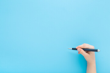 Baby boy hand holding black pen and writing on light blue table background. Pastel color. Closeup. Empty place for text. Top down view.