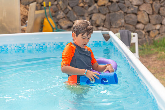 Smiling boy with water noodles in a pool, enjoying a sunny day outdoors
