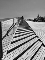 A serene wooden walkway winding through a tranqui lbeach with a person strolling. The lush greenery...