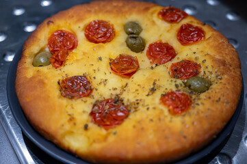 Tasty italian vegetarian food, fresh baked flat foccachia bread with cherry tomatoes, olives and herbs close up
