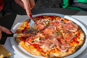 Eating of fresh baked pizza dish in italian pizzeria restaurant, Prosciutto di Parma