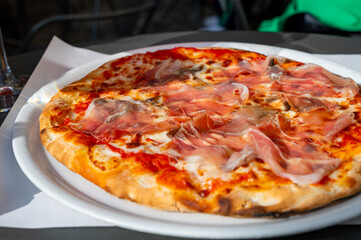 Eating of fresh baked pizza dish in italian pizzeria restaurant, Prosciutto di Parma