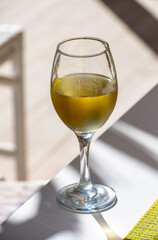 Glass of cold white wine on white terrace table outdoor in sunny day