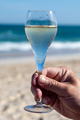 Hand with glass of cava or champagne sparkling wine on vacation, Dunes Corralejo sandy beach,...