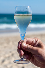 Hand with glass of cava or champagne sparkling wine on vacation, Dunes Corralejo sandy beach, Fuerteventura, Canary islands