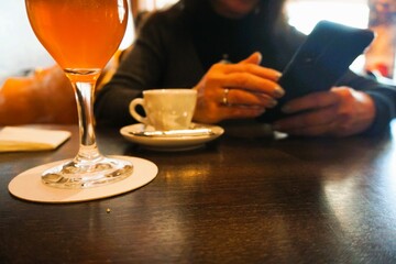 Frau sitzt am Tisch mit weißer Tasse Kaffee und Cocktailglas und hält Handy in ihren Händen in...