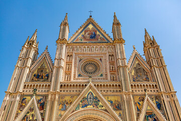 The facade of Orvieto Cathedral, Duomo di Orvieto, Umbria, Italy. Golden frontage, which is decorated by large bas-reliefs and statues with the symbols of the Evangelists. - obrazy, fototapety, plakaty