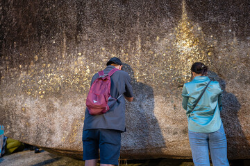 Male and women tourists pay their respects by covering the giant rocks with gold leaf at Khao Khitchakut National Park, Chanthaburi, Thailand.