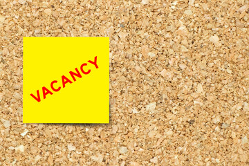 Yellow note paper with word vacancy on cork board background with copy space