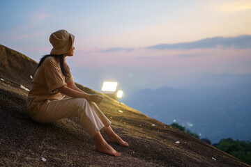 Woman at the edge of a cliff is looking at a beautiful sunset landscape.
