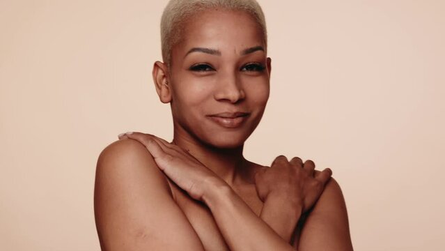 A joyful mixed race woman with a short hairstyle turns over her shoulder, covered by hands, exuding confidence and femininity on a neutral background.