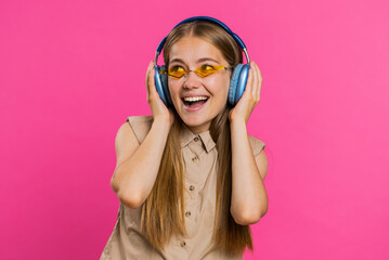 Happy woman in headphones listening music and dancing disco fooling around having fun expressive gesticulating hands relaxing on party. Blonde girl in sunglasses isolated on studio pink background
