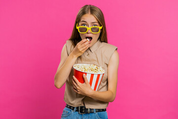 Excited young woman in 3D glasses eating popcorn and watching interesting tv serial, sport game, film, online social media movie content. Blonde lovely girl isolated on pink studio background