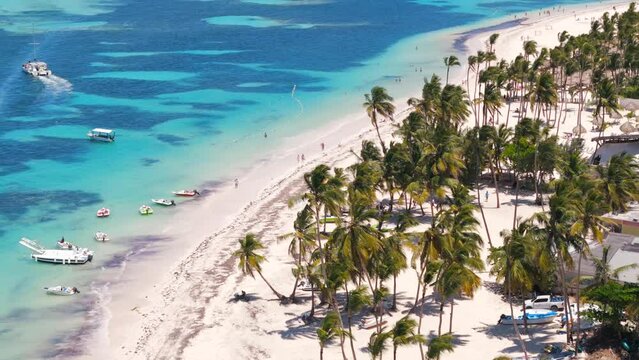 Aerial flight above white sand beach with many all inclusive hotels in Punta Cana. Turquoise water, tall palm trees and straw umbrellas on the coast. Best place for summer vacations 
