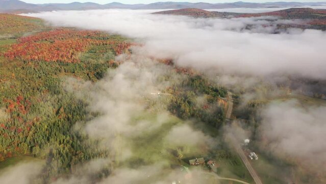 Drone flight through fluffy white clouds to forest, building and house. Mountains on the horizon.