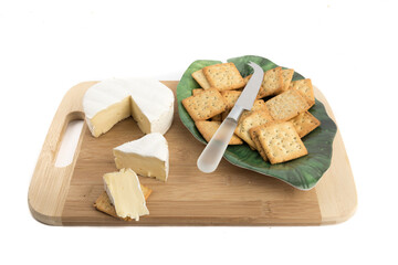 a round of brie cheese with a green plate of crackers on a wooden board isolated on white