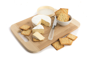 a round of brie cheese with a bowl of grain crackers on a wooden board isolated on white - Powered by Adobe