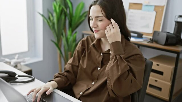 A young caucasian woman works attentively at her desk in a modern office setting, conveying professionalism and focus.